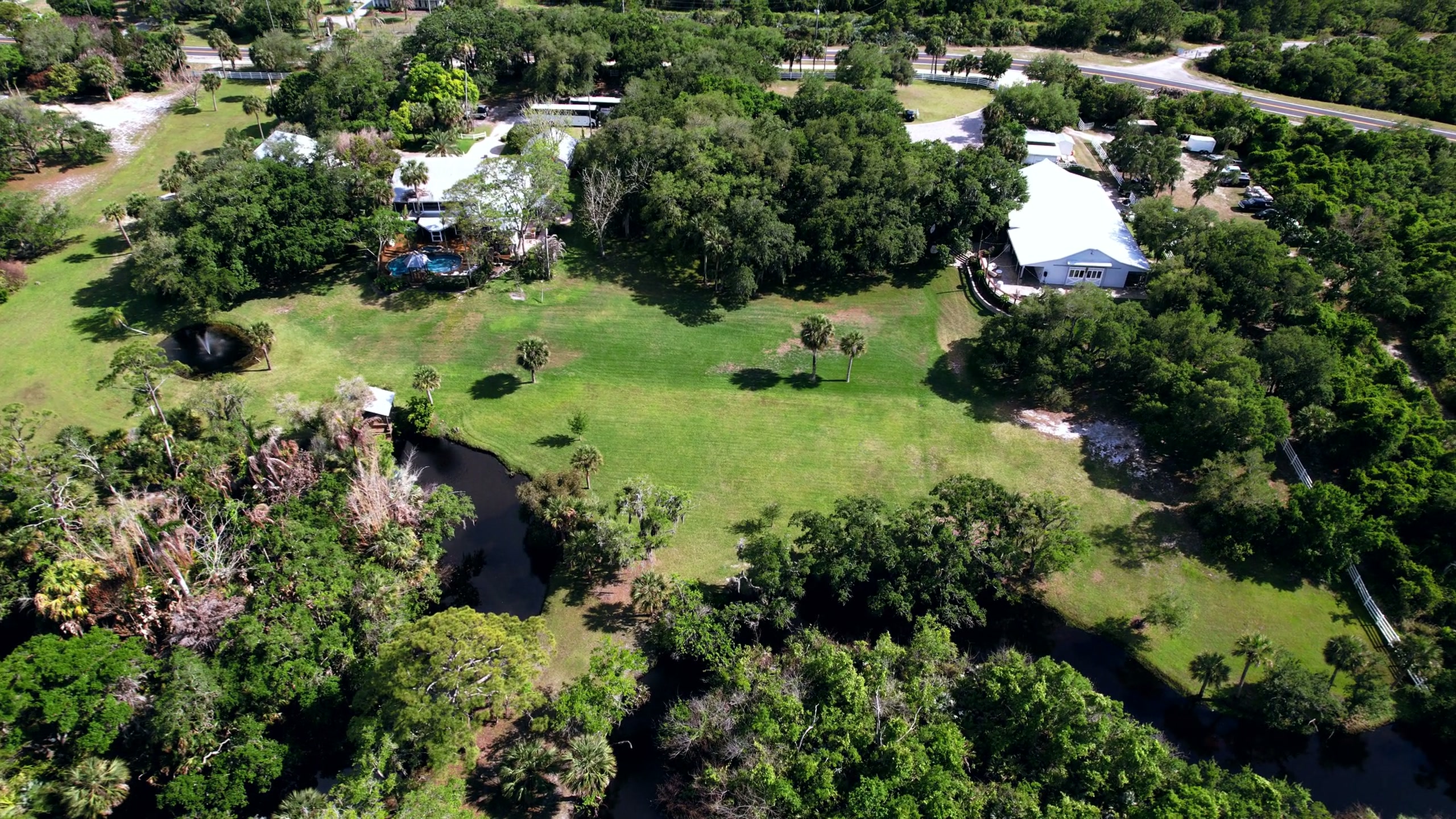 Aerial drone photograph of a Florida Space Coast property — lush green canopy, palms, and a small canal. Captured with FAA Part 107 certification.